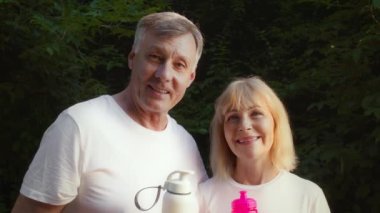 Emekli çifti sevmek birlikte kaliteli zaman geçirmek, parktaki kameralara gülümsemek, su dolu spor şişeleri taşımak