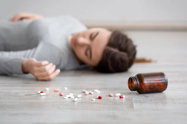 Blanke trieste duizendjarige vrouw die lijdt aan depressie pleegt zelfmoord, ligt bewusteloos, focus op pillen op de vloer — Stockfoto