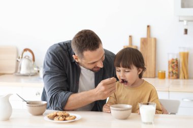 Çocukların beslenmesi. Sabahları oğlunu lapayla besleyen, çocuğuyla ilgilenen bir adam.