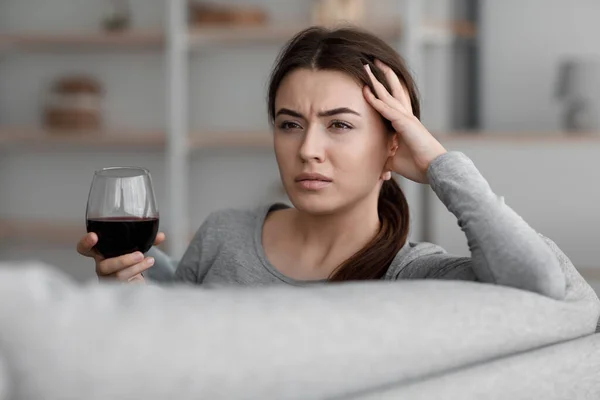 П'яна нещасна біла молода жінка з келихом вина, що страждає від депресії та головного болю і розслабляється вдома — стокове фото