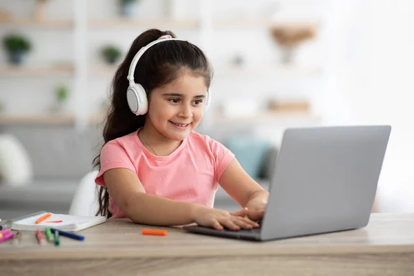Vzdálené učení. Malá arabská dívka ve sluchátkách studium doma s notebookem — Stock fotografie