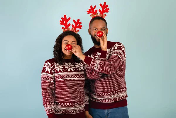 Pareja afroamericana muy alegre divirtiéndose con adornos navideños, sosteniéndolos cerca de las narices y usando cuernos de ciervo — Foto de Stock