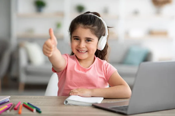 Online onderwijs. Klein meisje studeren met laptop thuis, Toont duim omhoog — Stockfoto