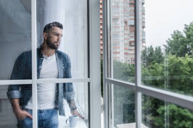 Depresyondaki üzgün adam pencereden bakıyor, salgının sona ermesini umuyor.