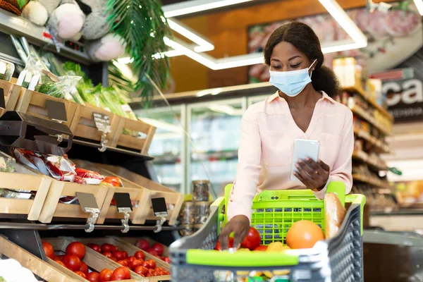 Black Lady Shopping Groceries Using Phone In Supermarket, Wearing Mask — Stock Photo, Image