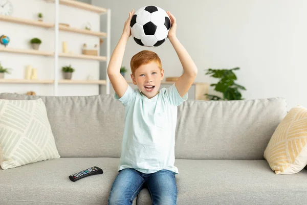 Emocional pelirrojo chico con bola viendo partido de fútbol en la televisión — Foto de Stock