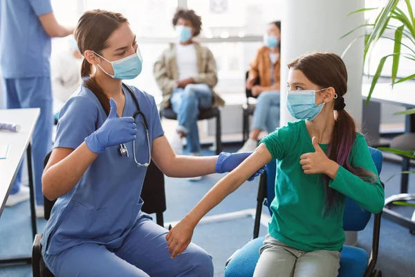 Vacunado chica y enfermera gestos pulgares hasta en la clínica — Foto de Stock