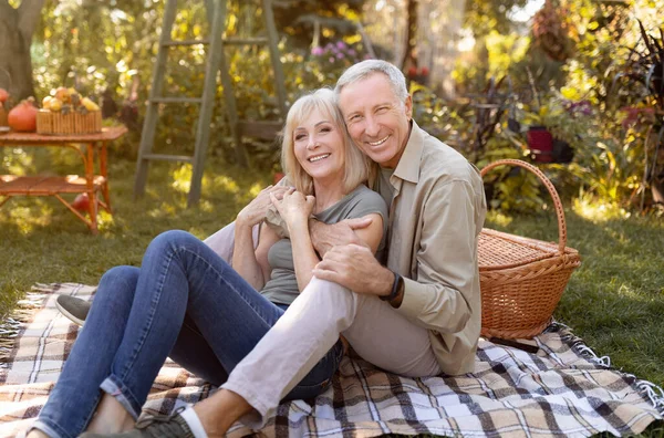 Amar pareja de ancianos descansando y haciendo picnic en el jardín, abrazando y sonriendo a la cámara, sentados juntos al aire libre —  Fotos de Stock