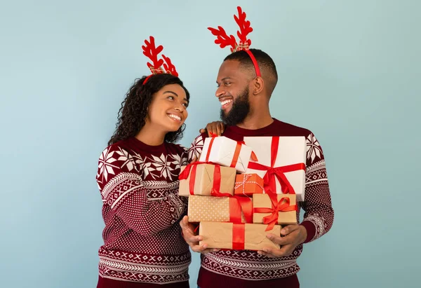 Святкування Нового року. Люблячі афроамериканські подружжя в светрах і рогах оленів, чоловік, який тримає купу різдвяних подарунків. — стокове фото
