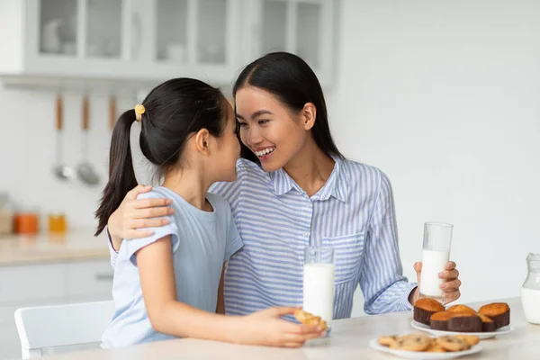 Mutlu Asyalı anne ve küçük kız mutfaktaki abur cuburları yiyorlar, sütle lezzetli kurabiyelerin tadını çıkarıyorlar. — Stok fotoğraf
