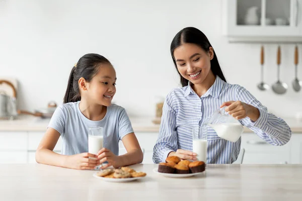 Junge asiatische Frau gießt Kalziumgetränk in Gläser und beißt zusammen mit Tochter in Küche zu — Stockfoto