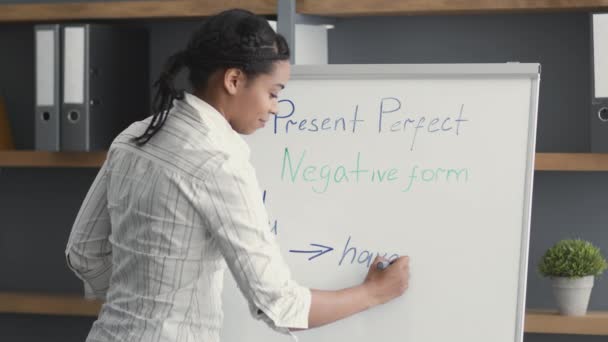 Joven profesional afroamericana profesora escribiendo reglas gramaticales en inglés en pizarra blanca, enseñando a los estudiantes — Vídeo de stock