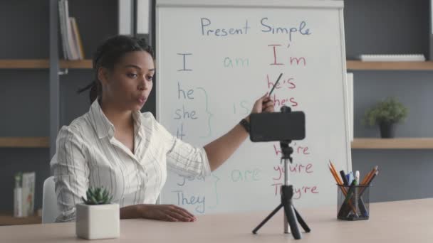 E-learning concept. Jonge Afrikaanse Amerikaanse dame leraar opnemen van Engels tutorial, praten met smartphone camera een — Stockvideo