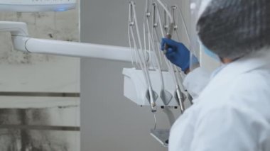 Koruyucu giysi ve yüz maskesi takan kadın dişçi diş malzemelerini alıyor ve siyah erkek hastayı tedavi etmeye başlıyor.