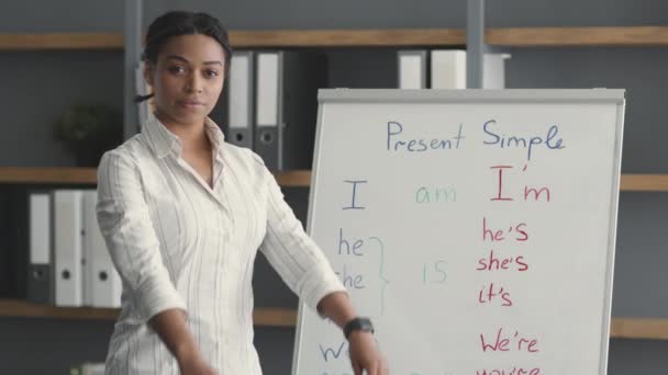 Concepto de educación en línea. Joven profesional confiado mujer afroamericana profesora posando cerca de pizarra blanca y sonriendo — Vídeos de Stock