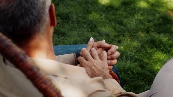 Casal sênior segurando as mãos enquanto relaxa na cadeira de vime ao ar livre, close-up — Vídeo de Stock