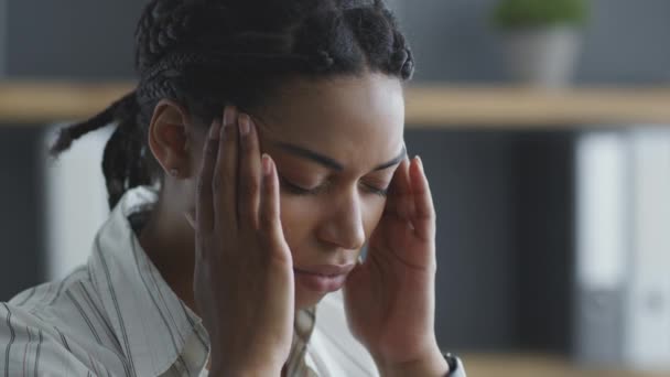 偏頭痛の概念。若い黒人女性のオフィスマネージャーは、仕事で彼女の寺院をマッサージし、急性頭痛に苦しんでいます — ストック動画