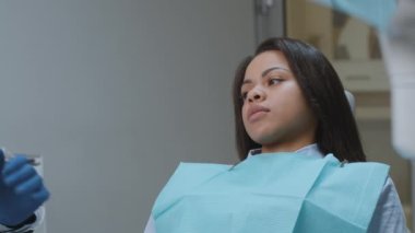 Dişçi korkusu. Genç, korkmuş Afrikalı Amerikalı kadın diş kliniğinde oturuyor ve doktorları aletlerle reddediyor.