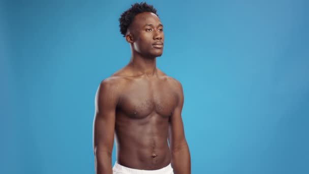 Sportos életmód. Stúdió lövés fiatal félmeztelen izmos afro-amerikai férfi pózol a kék háttér — Stock videók