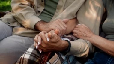 Bahçede dinlenirken kıdemli çiftin el ele tutuşurken çekilmiş yakın plan fotoğrafı.