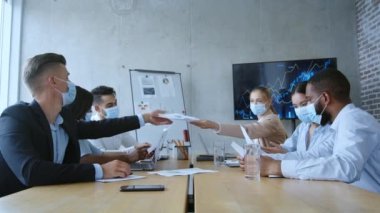 Salgın sırasında çevrimdışı çalışma. Koruyucu yüz maskeleri takmış çok ırklı meslektaşlar ofiste oturmuş projeyi tartışıyorlar.