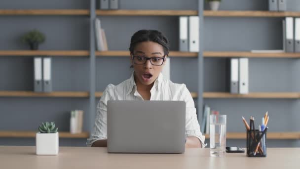 若いアフリカ系アメリカ人の女性マネージャーがノートパソコンで入力し、電子メールを獲得し、職場で喜んで踊ります — ストック動画