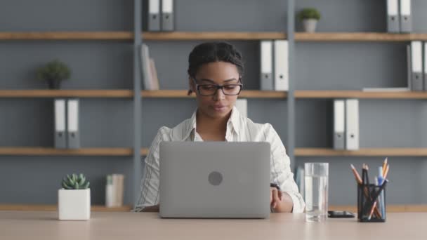 Νεαρή χαρούμενη γυναίκα αφροαμερικανός διευθυντής γραφείου δακτυλογραφεί στο lap-top, τελειώνοντας την εργασία και το κλείσιμο του υπολογιστή — Αρχείο Βίντεο