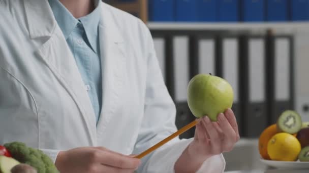 Υγιείς διατροφικές συμβουλές. Νεαρή επαγγελματίας γιατρός μιλάει με ασθενή στο γραφείο, δείχνει πράσινο φρέσκο μήλο — Αρχείο Βίντεο