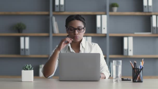 Mujer afroamericana agotada joven sintiéndose cansada en el lugar de trabajo, trabajando en el ordenador portátil horas extras en la oficina — Vídeo de stock