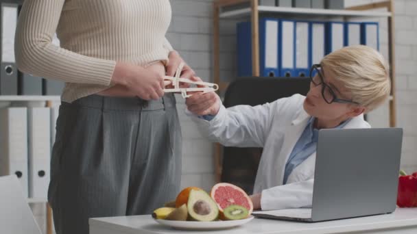 Arzt Ernährungsberater misst Körperfettindex für junge Patientin, bevor er Behandlungsplan aufstellt, sitzt im Büro — Stockvideo