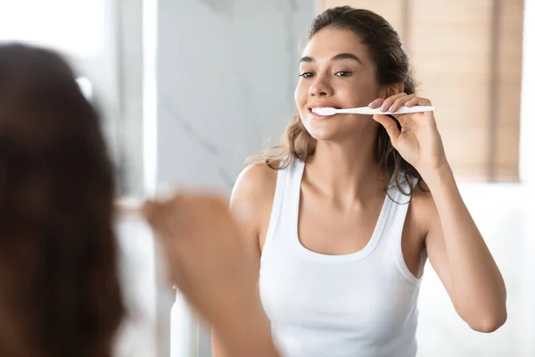 Веселая женщина чистит зубы и делает зубной уход рутина в ванной комнате — стоковое фото