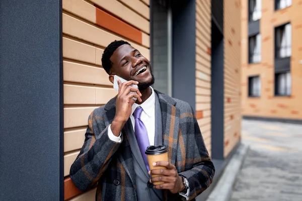 Щасливий чорний бізнесмен розмовляє на мобільному телефоні під час перерви, гуляючи по місту і п'ючи каву, вільне місце — стокове фото