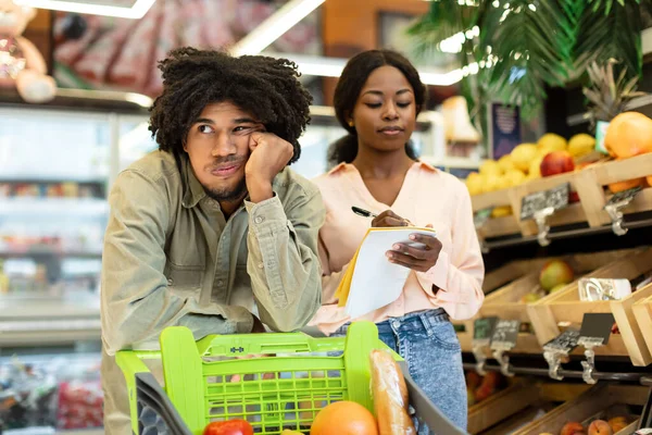 Uttråkad afrikansk make väntar fru under matinköp i snabbköpet — Stockfoto