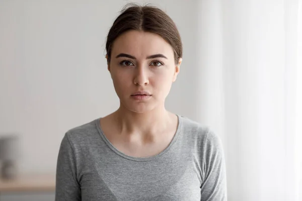 Sad unhappy european millennial woman suffering from depression and looking at camera at home interior