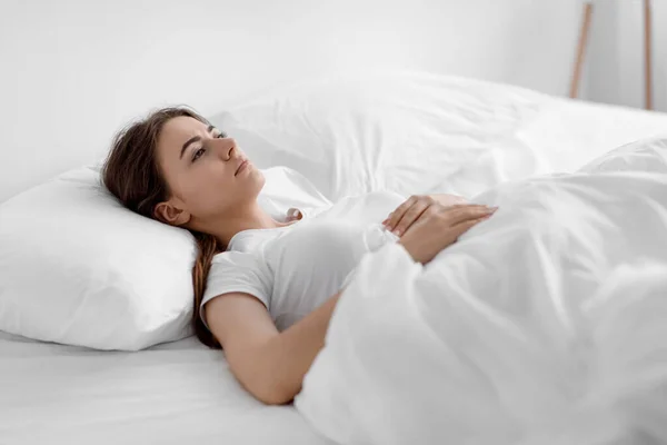 Stanca triste sconvolta europea millenaria donna che soffre di depressione e stress, sdraiata sul letto bianco a casa — Foto Stock