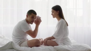 Yatakta yan yana oturan genç çift domuzcuk kumbarasını sallıyor.