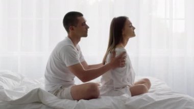 Değer veren bir adam yatakta karısına rahatlatıcı vücut masajı yapıyor.