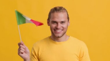 İtalya bayrağıyla el sallayan ve kameraya bakan genç bir adam.