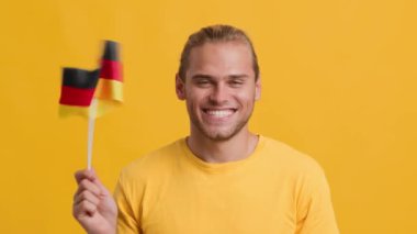 Neşeli vatansever milenyum adamı sarı arka planda Alman bayrağı sallıyor.