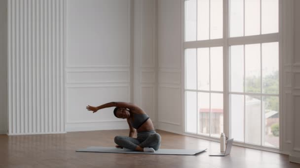 Jonge zwarte vrouw zitten in lotus positie en stretching lichaam naar zijkanten — Stockvideo