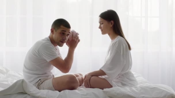 ベッドで一緒に座っている間に若いカップル揺れ貯金箱を動揺 — ストック動画
