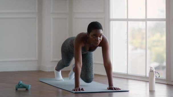 Sportig svart kvinna utbildning hemma, gör knä till bröstet Plank Motion — Stockvideo