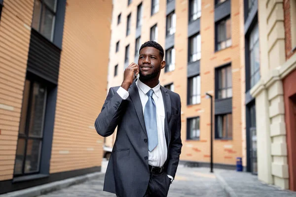 Affärssamtal. Glad afrikansk amerikansk affärsman talar på smartphone, promenader i staden mot office center — Stockfoto