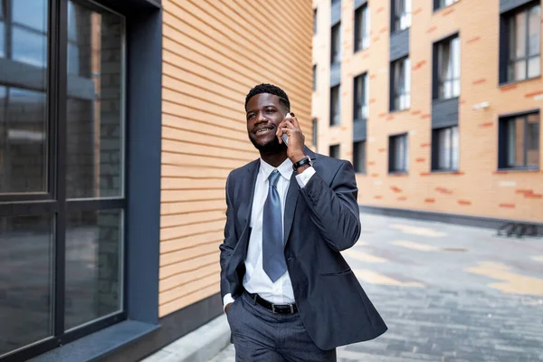 Spännande afrikansk amerikansk affärsman talar på smartphone, promenader utomhus nära moderna kontorshotell, kopiera utrymme — Stockfoto