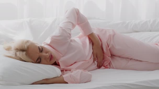 Menstruationssmärta. Sjuk ung blond kvinna röra Belly när du ligger i sängen — Stockvideo