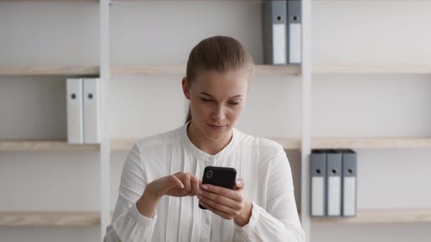 O tânără femeie de afaceri care utilizează smartphone-ul la locul de muncă în timp ce are pauză la birou — Videoclip de stoc