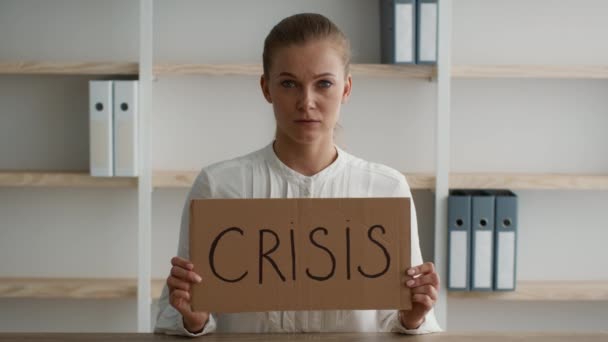 Расстроенная молодая женщина, держащая плакат с надписью о кризисе за столом в офисе — стоковое видео