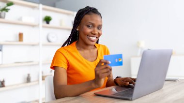 E-ticaret. Milenyum Afrikalı Amerikalı kadın uzaktan ödeme için kredi kartı kullanıyor, evde bilgisayarla alışveriş yapıyor.