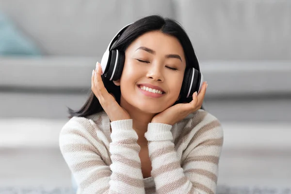 Nahaufnahme einer schönen Asiatin, die Musik in drahtlosen Kopfhörern hört — Stockfoto