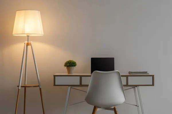 흰색 의자, 빈 화면 이 있는 노트북, 탁자 위에 화분 식물, 저녁에는 회색 벽 배경에 빛나는 램프 — 스톡 사진